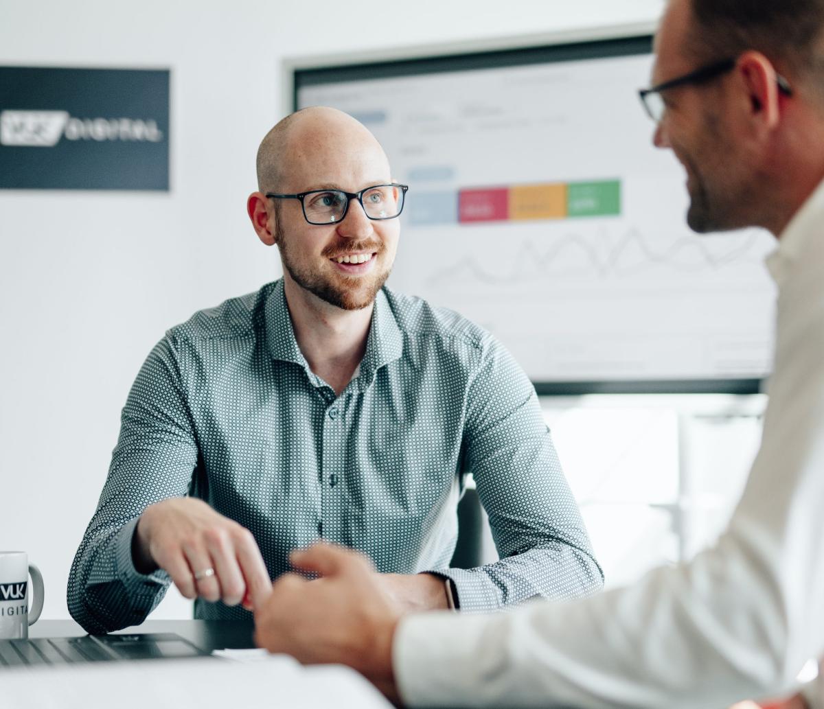 Zwei Männer diskutieren über Marketing für Sachverständige in einem Büro.