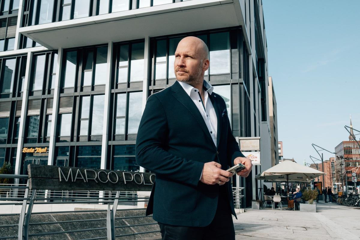 Mann in Anzug steht vor einem modernen Gebäude, während er sein Handy hält und nachdenklich wirkt, passend zur privaten Krankenversicherung im Alter.