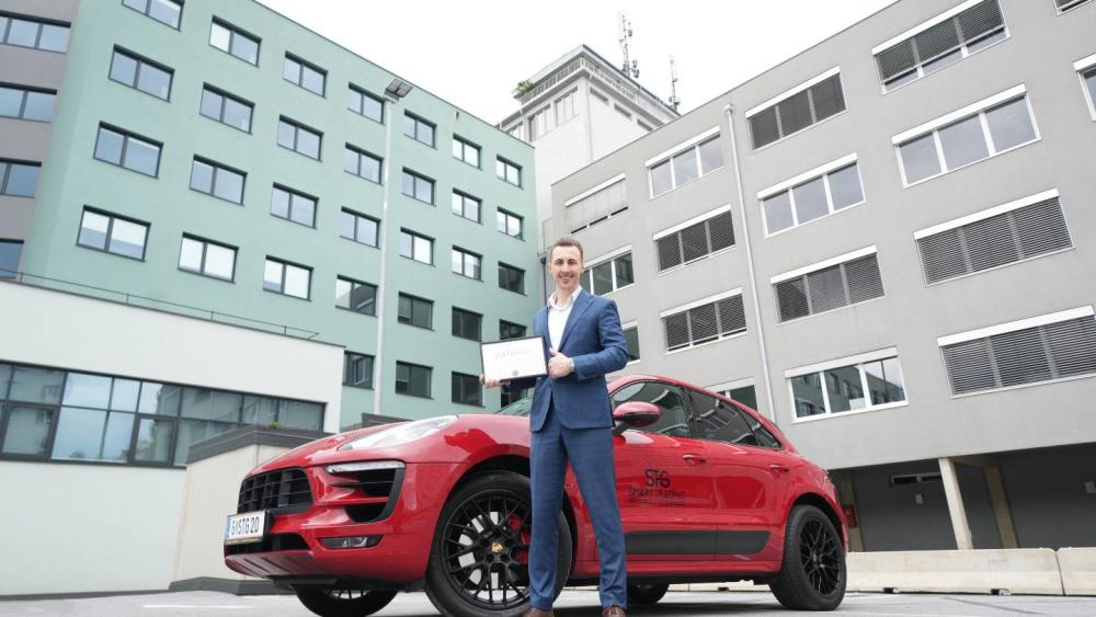 Thomas Wabnig präsentiert das beste Trading-Ausbildung-Angebot in Österreich vor einem roten Auto.