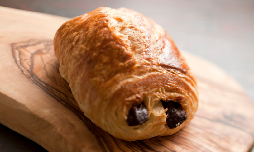 Ein schokoladiges Croissant auf einem Holzbrett, das den Fokus auf Abnehmen ohne Verzicht symbolisiert.