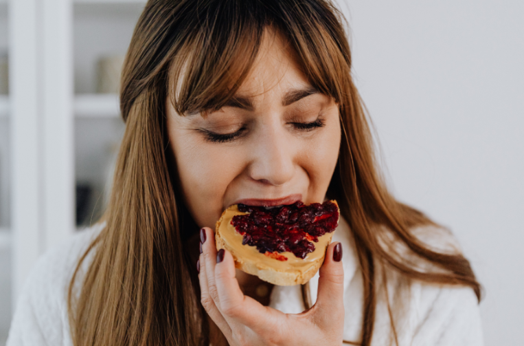 Frau isst ein Brot mit Marmelade als Teil einer Ernährungsstrategie bei Schilddrüsenunterfunktion.
