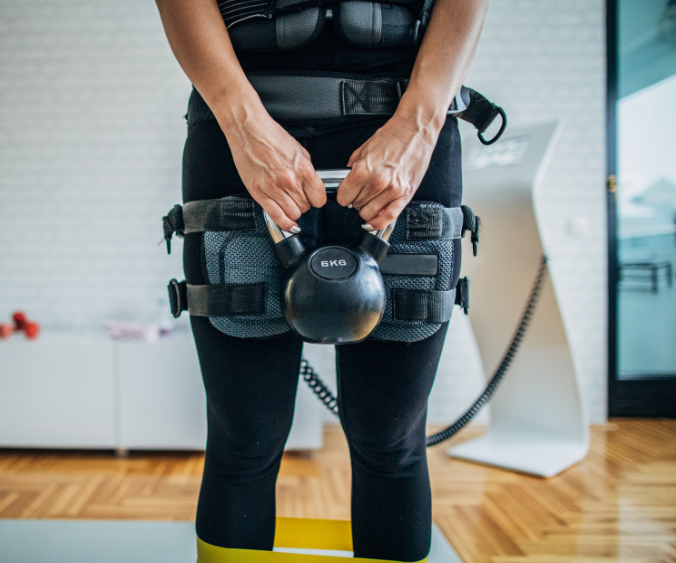 Frau in EMS-Anzug mit Kettlebell beim Abnehmen und EMS-Training.