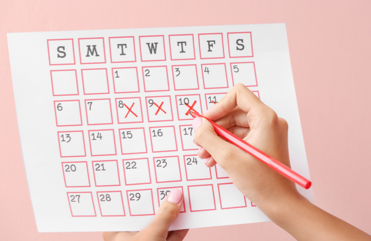 Eine Hand markiert den Menstruationszyklus in einem Kalender mit dem Fokus auf den Zyklus verstehen.