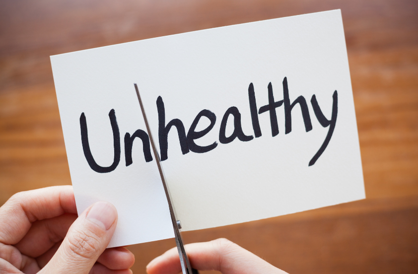 Eine Karte mit dem Wort 'Unhealthy', die geschnitten wird, symbolisiert gesunde Ernährung beim Abnehmen.