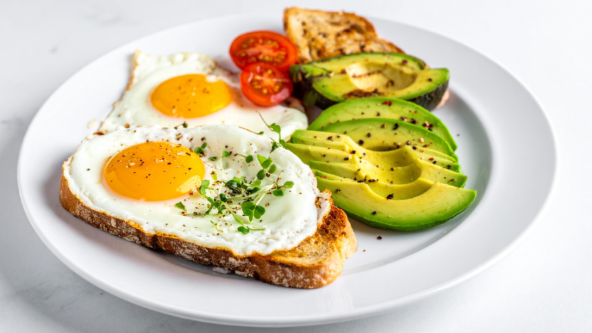 Ein gesundes Frühstück mit zwei Spiegeleiern, Avocado und Tomaten als Teil der Strategie gegen Heißhunger.