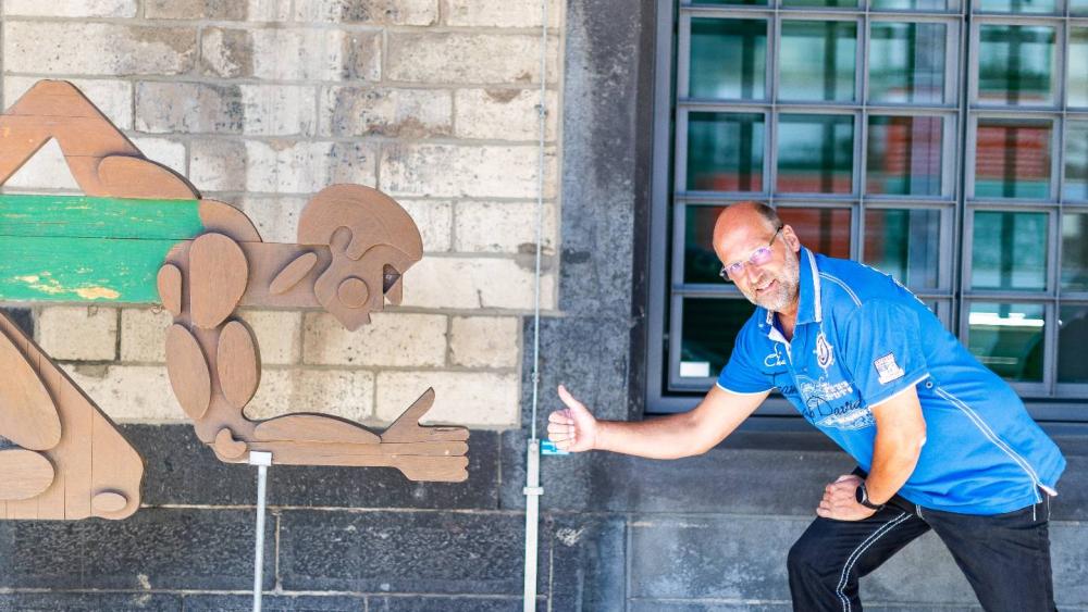Mitarbeiter in blauem Poloshirt zeigt auf eine Wanddekoration im Eingangsbereich eines Betriebs zur betrieblichen Krankenversicherung.