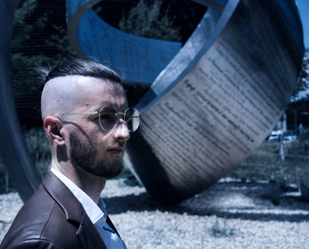 Mann mit Brille steht vor einer metallischen Skulptur zum Thema Manifestieren.