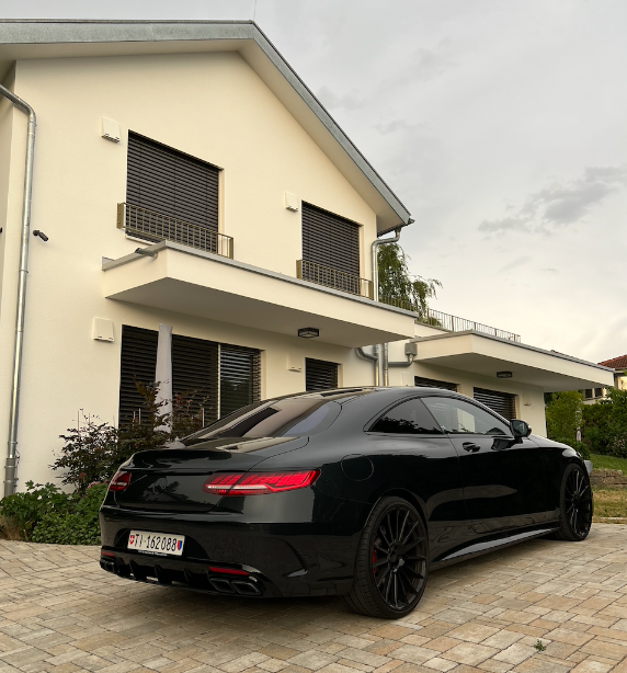 Ein schwarzes Luxusauto parkt vor einer modernen Villa.