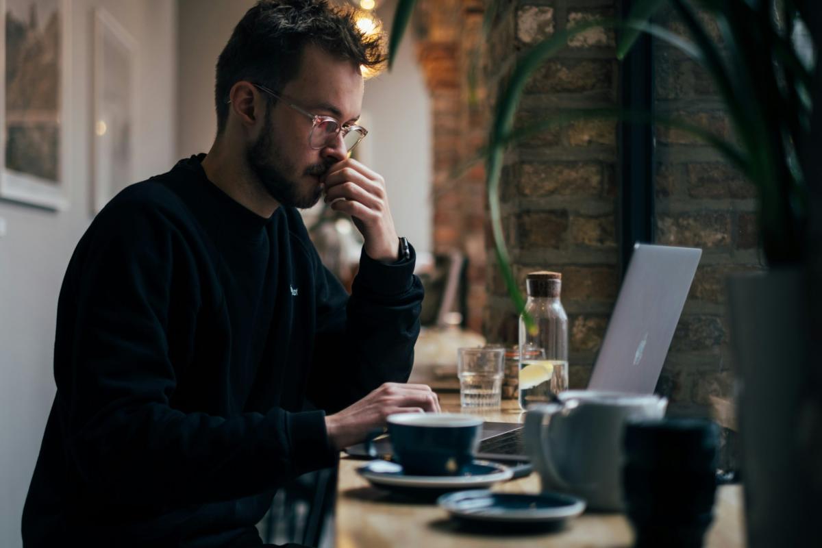 Mann arbeitet konzentriert am Laptop in einem Café, träumt von einem KI-Agenten im Unternehmen.