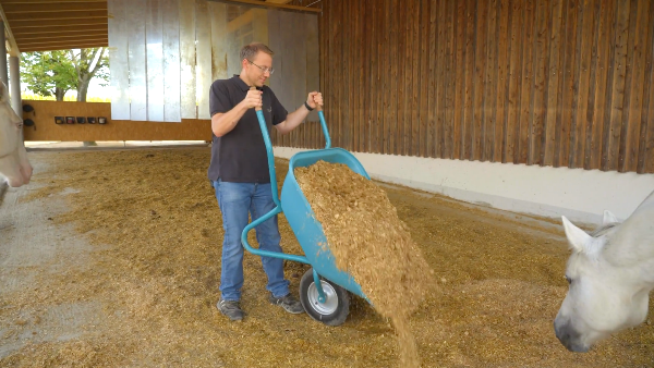 Ein Landwirt schüttet Strohpellets in einen Pferdestall für eine effiziente Einstreu.