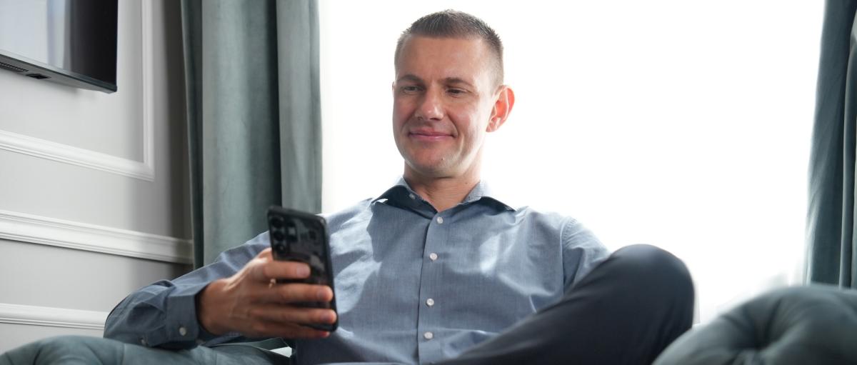 Mann sitzt entspannt auf Sofa und schaut auf sein Handy, Matthias Neumann Erfolgsmethode.