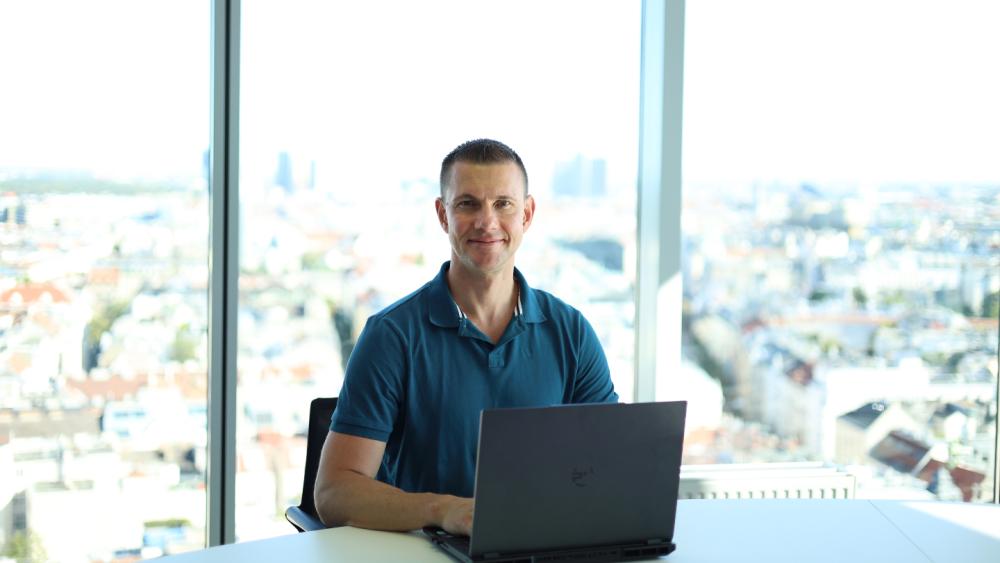 Ein Mann sitzt am Arbeitsplatz mit Laptop und blickt auf die Stadt, Texte schreiben lernen.