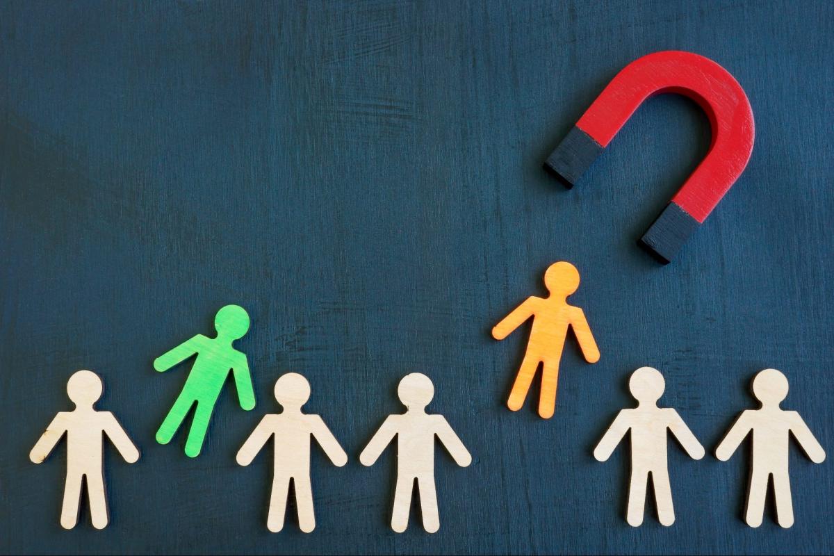 Ein Magnet zieht eine orangefarbene Figur zu einer Gruppe von Menschen im Recruiting-Kontext.