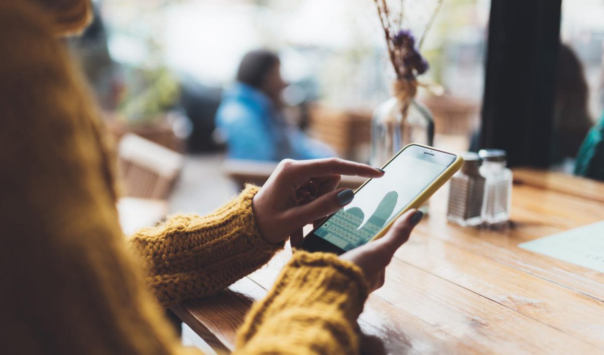 Eine Person tippt auf ihrem Smartphone, während sie im Café sitzt und die Sichtbarkeit ihres Unternehmens steigert.