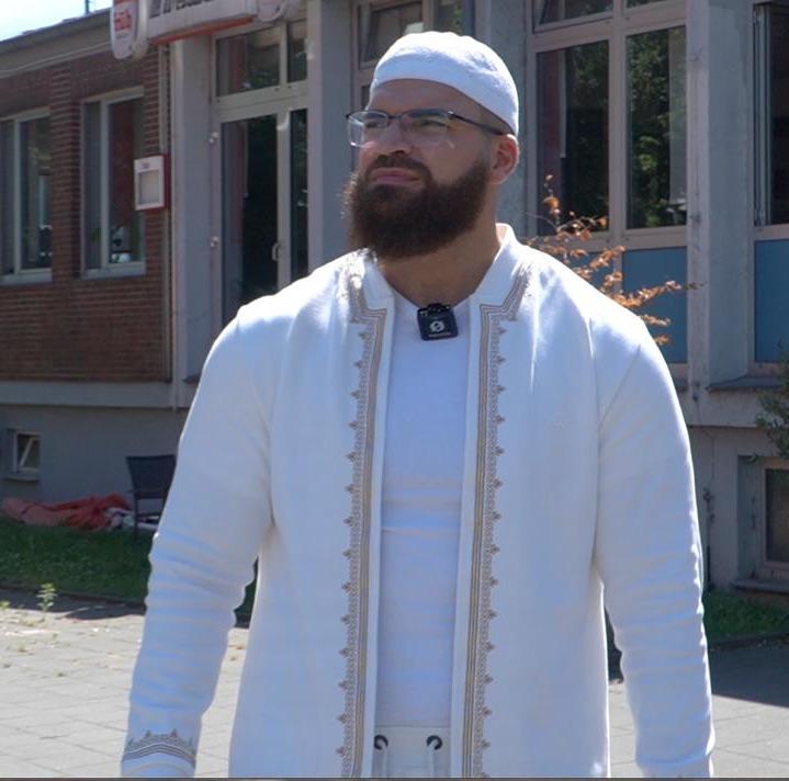 Mann in traditioneller weißer Kleidung steht draußen und genießt den Tag.