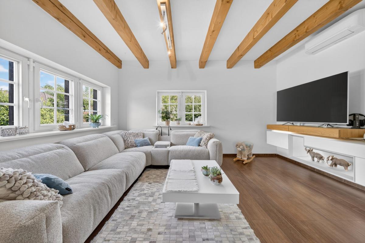 Helles Wohnzimmer mit Holzdeckenbalken und moderner Möblierung in professioneller Immobilienfotografie.