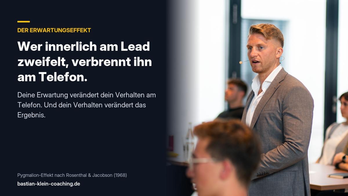 Finanzberater spricht im Büro am Telefon, während im Hintergrund weitere Personen an ihrem Arbeitsplatz sitzen.