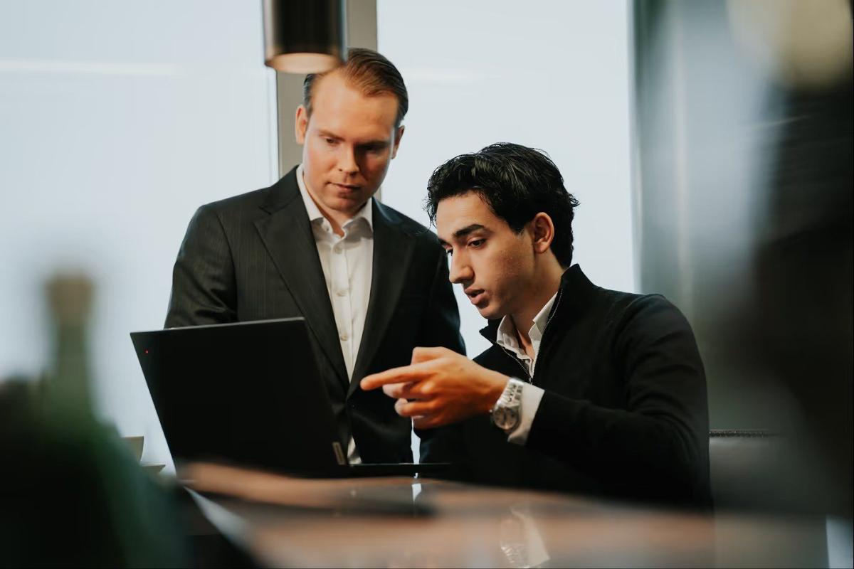 Zwei Mitarbeiter besprechen den Unternehmensverkauf Prozess am Laptop.