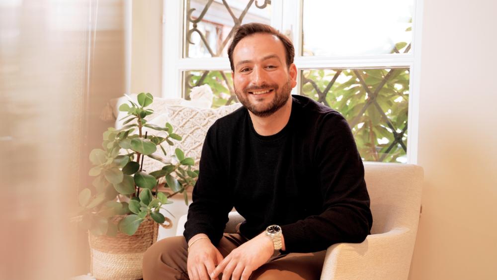 Ein Mann sitzt auf einem Sofa und lächelt, während er über das Thema 'zu nett als Chef' nachdenkt.