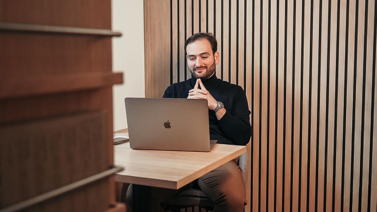 Ein Chef sitzt am Tisch vor einem Laptop und überlegt, wie er sich besser durchsetzen kann.