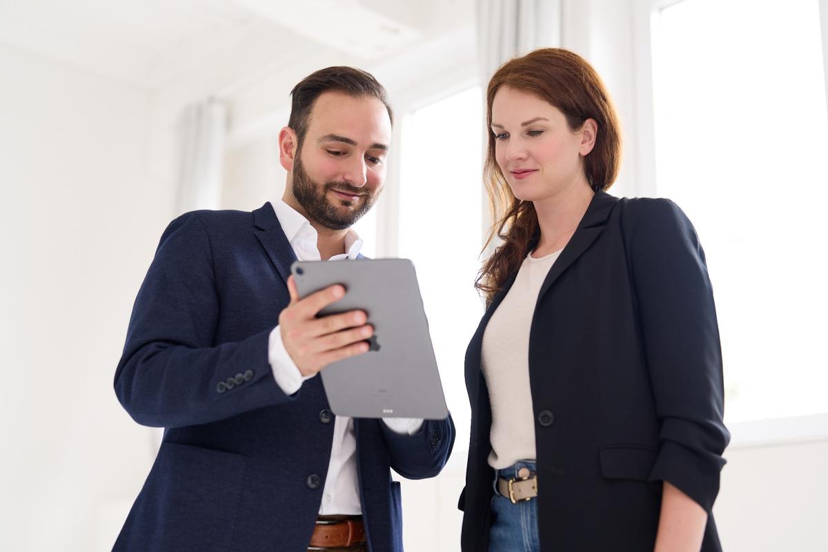 Zwei Personen diskutieren über verbindliche Führung und sehen auf ein Tablet.