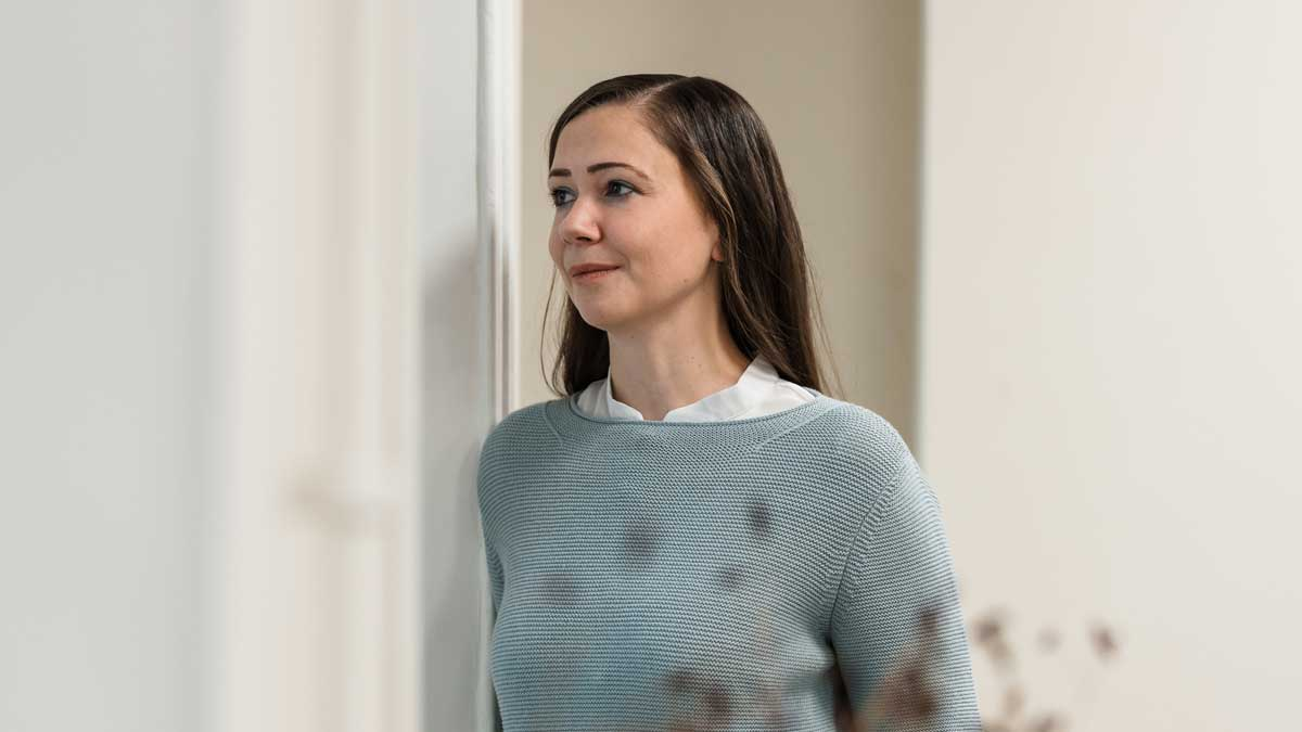 Eine Frau steht nachdenklich in einem Raum und reflektiert über Verkaufsfähigkeit in der Vermögensverwaltung.