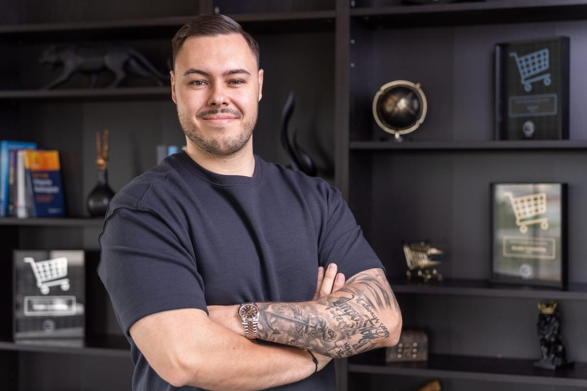 Mann mit Tattoos steht selbstbewusst vor Regalen und präsentiert Tipps zur Onlineshop-Optimierung.
