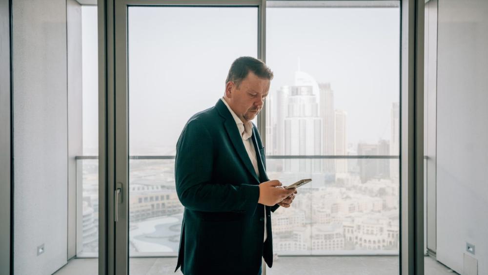 Mann mit Smartphone in Dubai, der über Zinsen bei Bauträgern informiert.