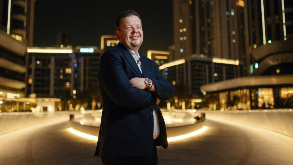 Ein beratender Mann steht vor der beleuchteten Skyline von Dubai und spricht über Dubai Immobilien.