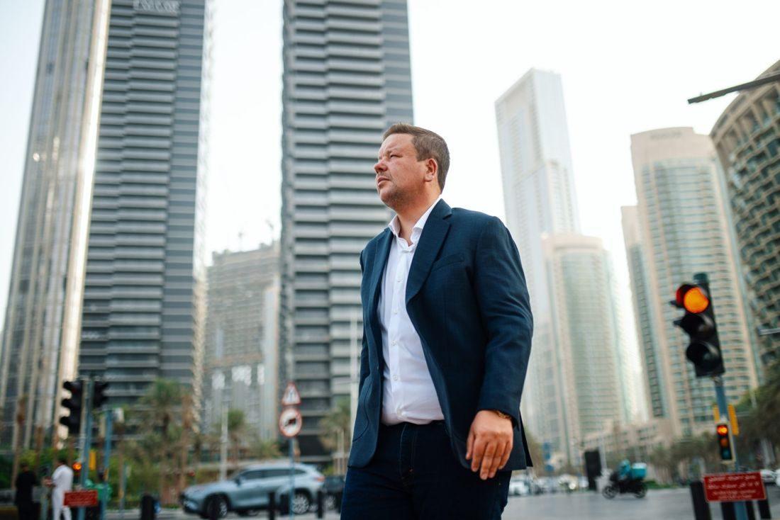 Mann in Anzug steht in Dubai zwischen modernen Hochhäusern, während er über Immobilienkauf nachdenkt.