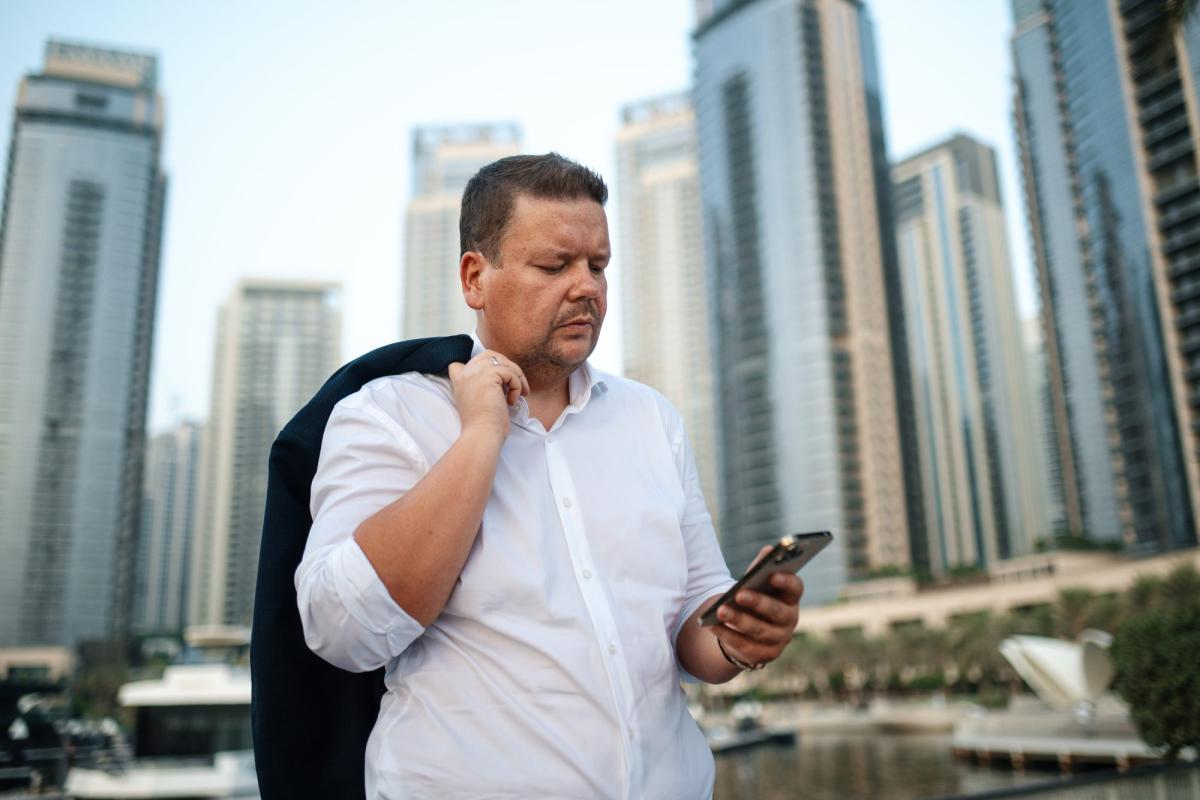 Mann liest auf Smartphone Informationen zur Mietrendite in Dubai vor Wolkenkratzern.