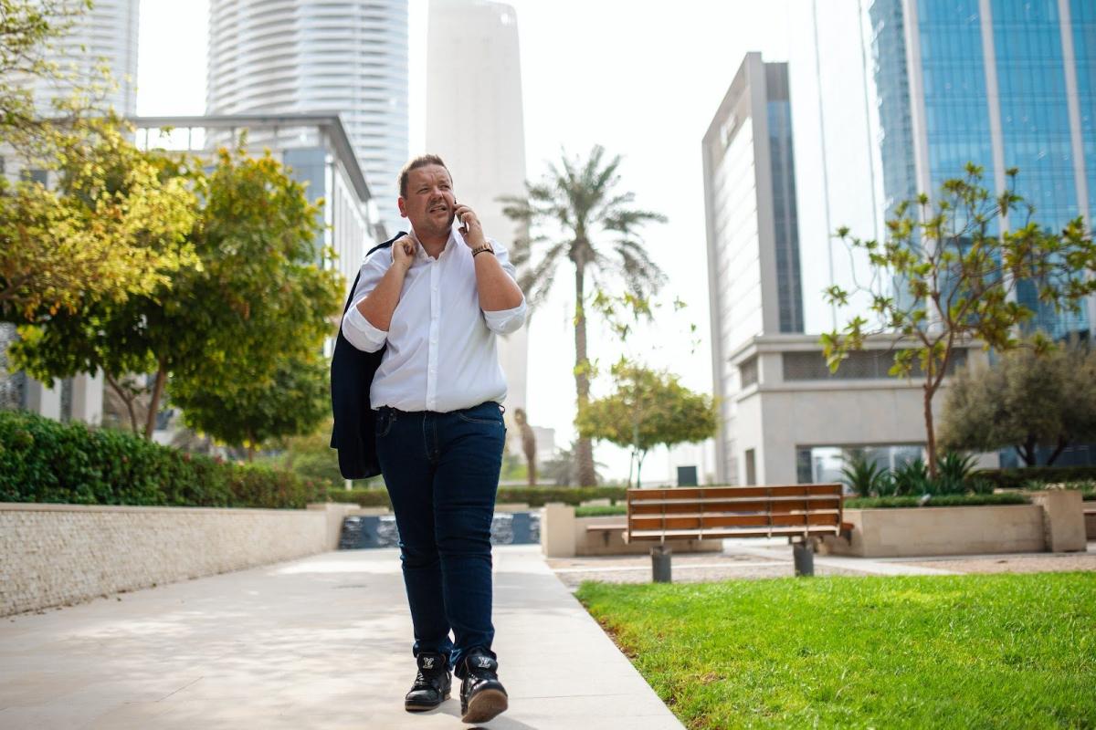 Ein Mann telefoniert auf einem Weg zwischen modernen Hochhäusern; Thema: Dubai Immobilie finanzieren.
