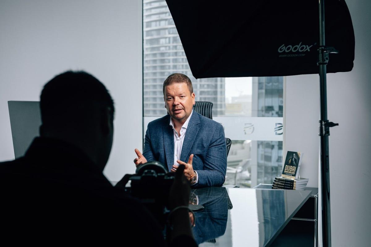 Dubai Immobilienfinanzierung im Interview: Ein Mann spricht vor der Kamera in einem hellen Büro.