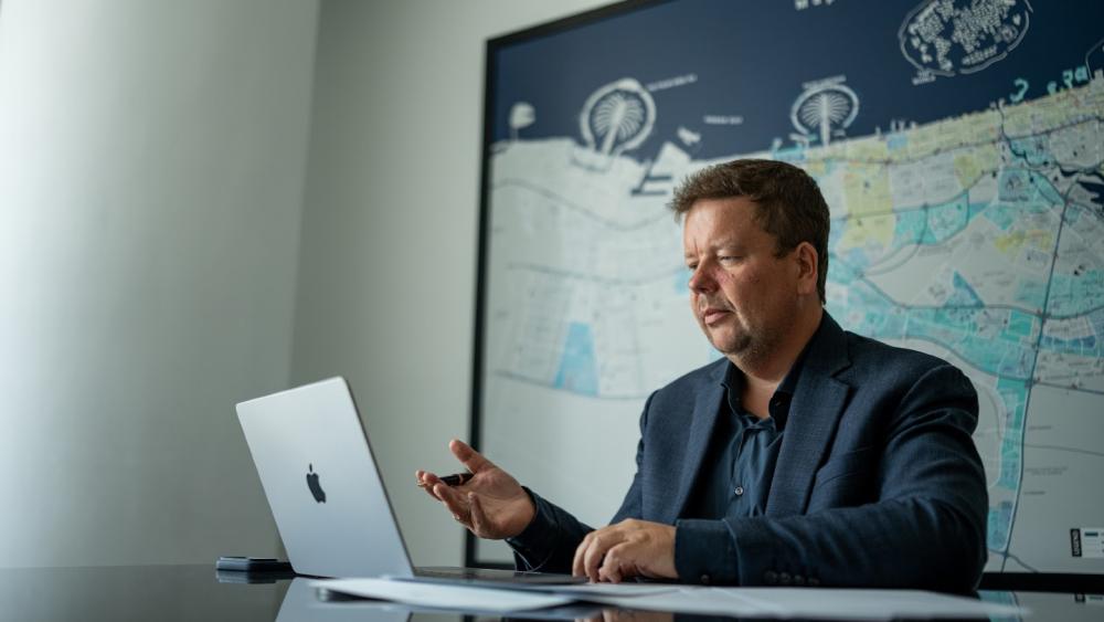 Dubai Immobilie Finanzierung: Ein Berater sitzt am Laptop vor einer großen Weltkarte und erklärt etwas.
