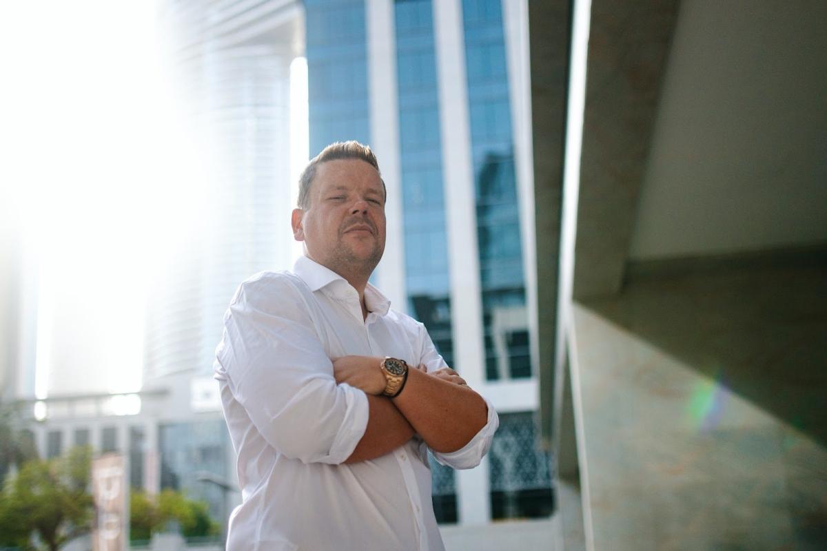 Eugen Zimbelmann steht vor modernen Gebäuden in Dubai und berät Immobilieninvestoren.