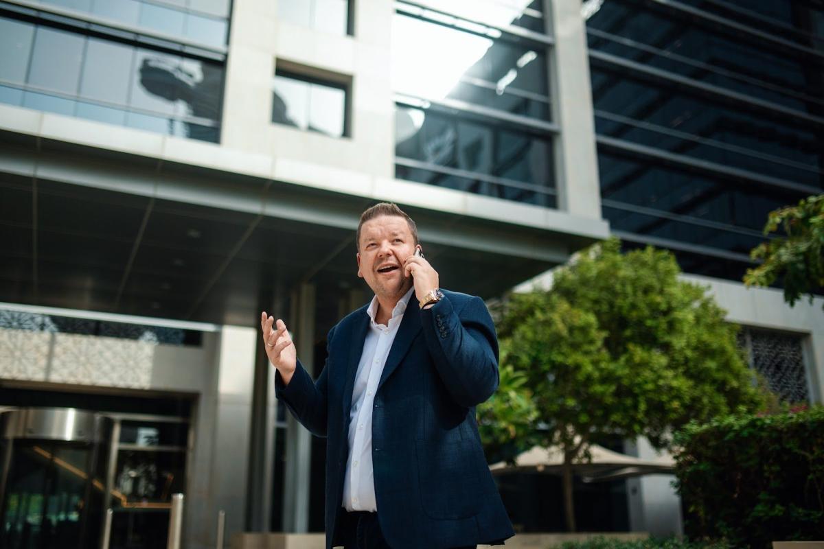 Mann telefoniert vor einem modernen Bürogebäude in Dubai, Thema: RERA-Mietindex.
