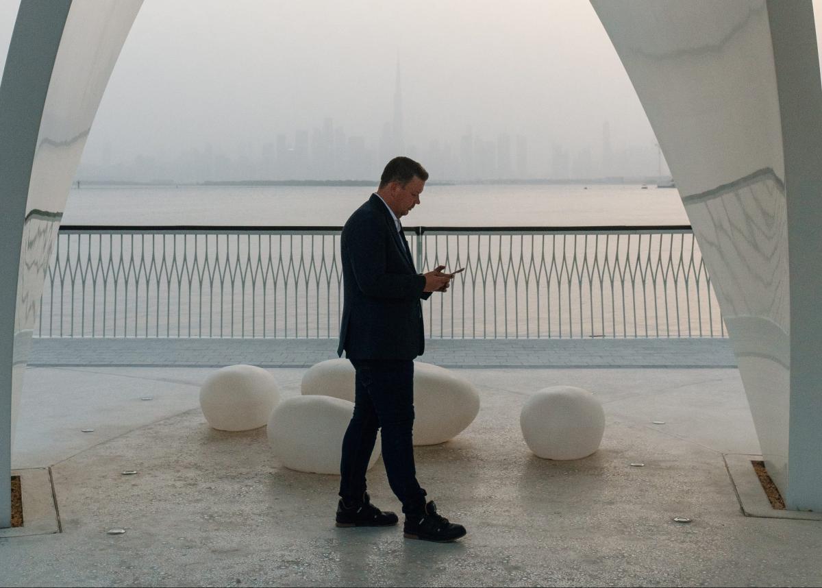 Mann steht unter einer Brücke und betrachtet sein Handy am Dubai Immobilienmarkt 2026.