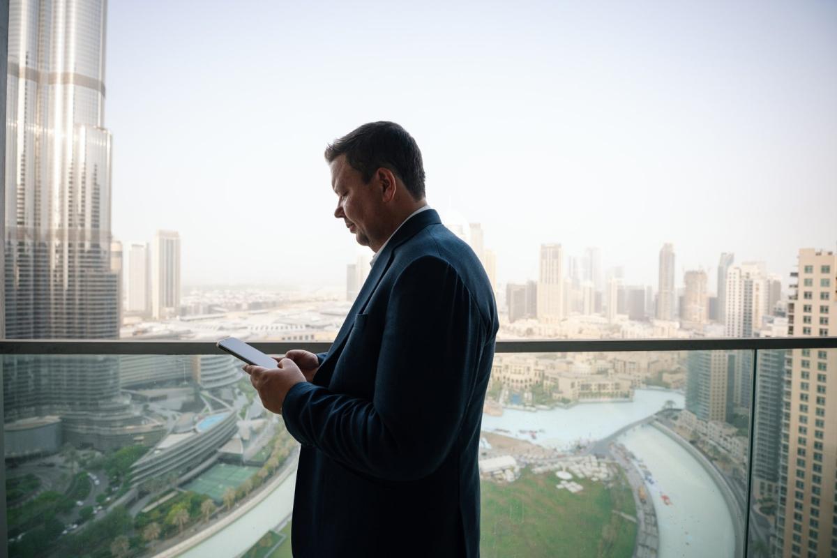 Mann in Anzug schaut auf sein Smartphone und blickt auf Dubai.