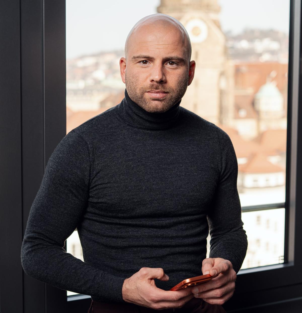 Mann mit Smartphone am Fenster, bereit für die Kaltakquise ohne Angst.