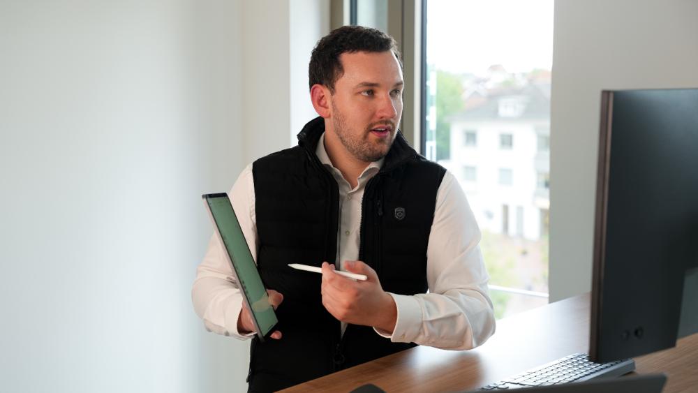 Ein Mitarbeiter sitzt mit grünem Ordner am Schreibtisch neben einem Monitor – IT-Sicherheit im Arbeitsalltag.