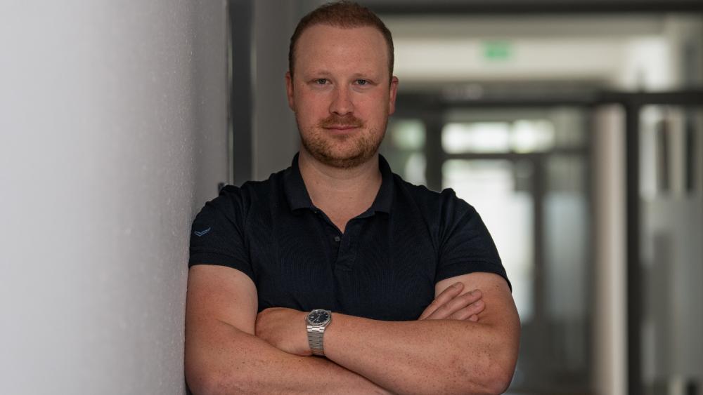 Ein Mann steht mit verschränkten Armen in einem modernen Büro und symbolisiert Hackerangriffe.