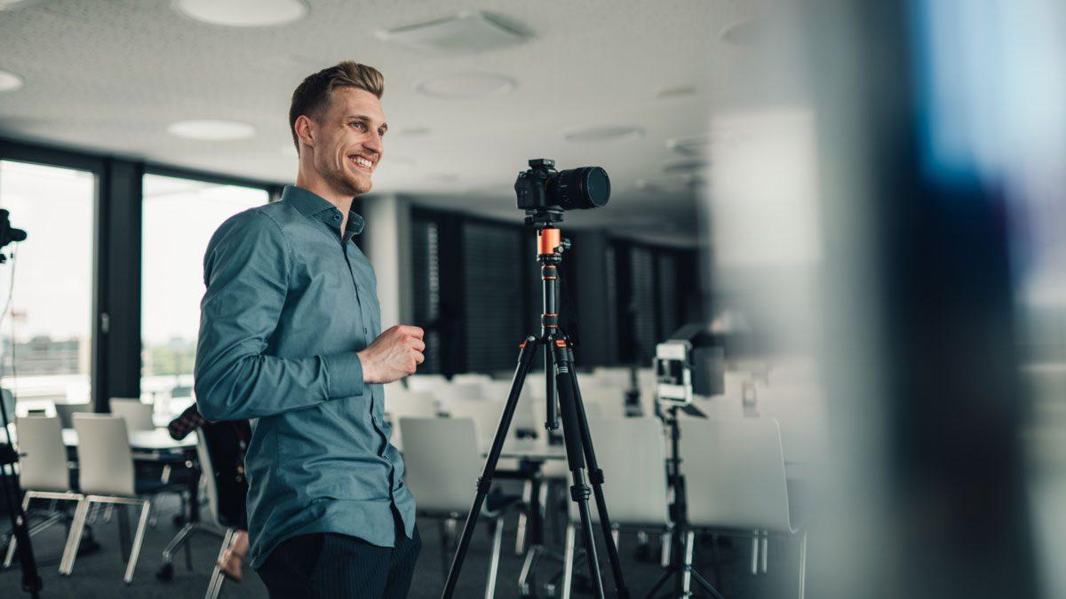 Ein Mann steht lächelnd vor einer Kamera während der Video-Testimonials-Dreharbeiten.