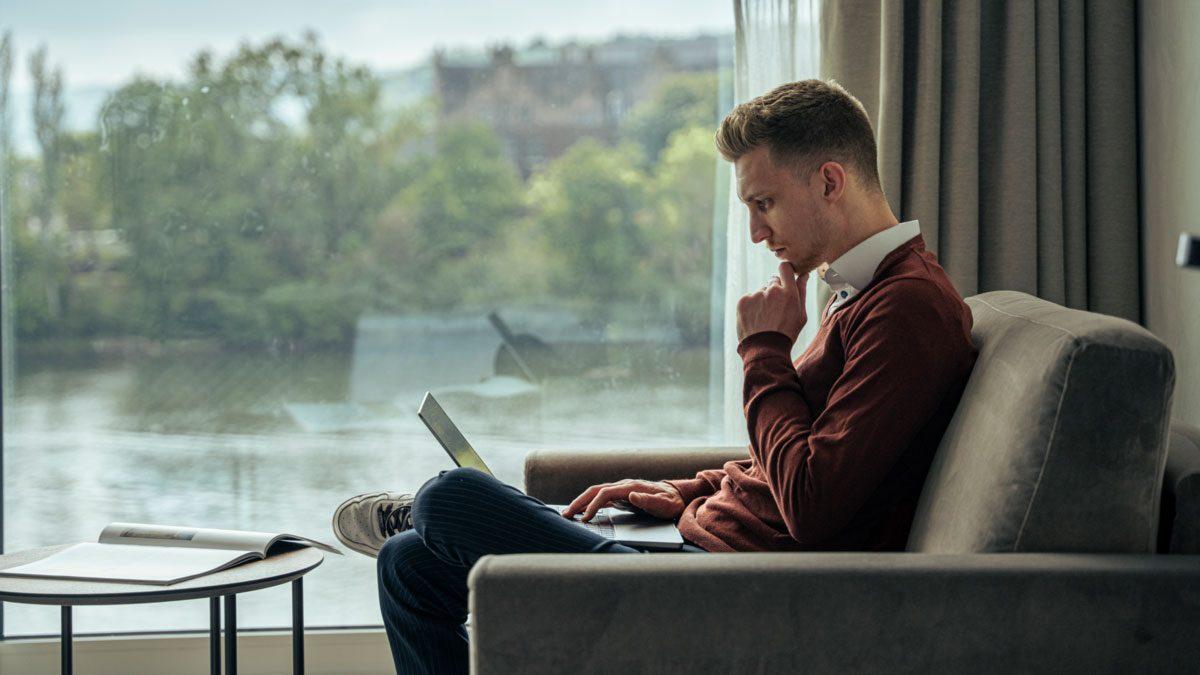 Mann sitzt im Wohnzimmer und arbeitet an einem Laptop zu Video-Testimonials im Marketing.