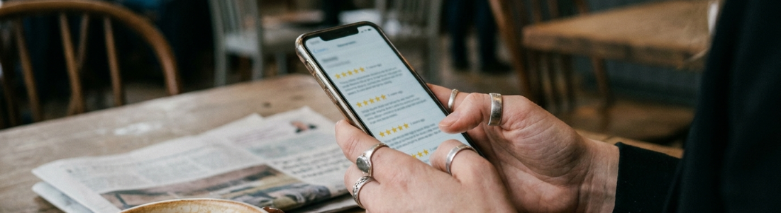Eine Hand hält ein Smartphone mit sichtbaren Kundenbewertungen, ideal um Kundenbewertungen sichtbar zu machen.