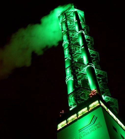 Beleuchteter Schornstein der Stadtwerke Duisburg mit grünem Licht.