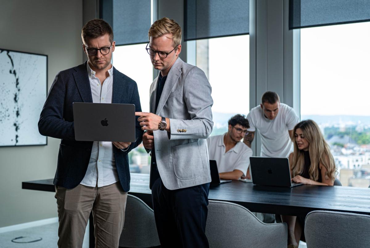 Zwei Männer diskutieren Werbebudget Strategien am Laptop in einem modernen Büro.
