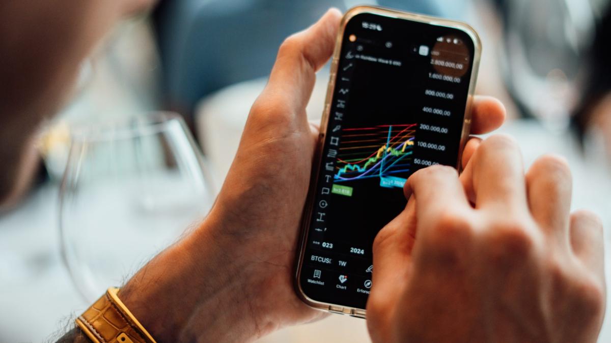 Person analysiert Trading-Daten auf dem Handy, während Florian Sondershausen seriös ist.