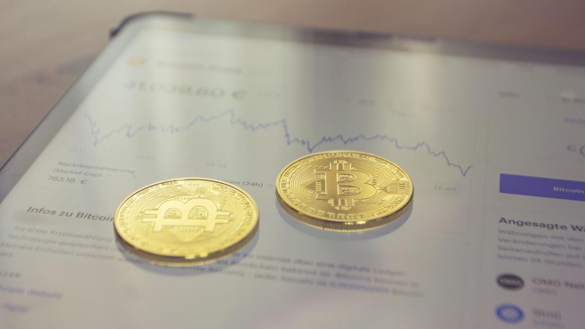 Zwei Bitcoin-Münzen auf einem Tablet mit Diagramm zu Kryptowährungen kaufen.
