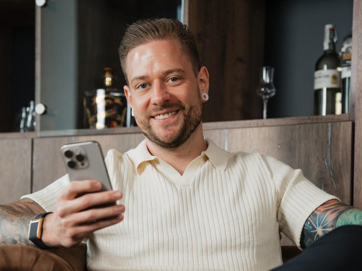 Mann mit Smartphone lächelt beim Lesen über den kostenlosen Einstieg ins Trading.