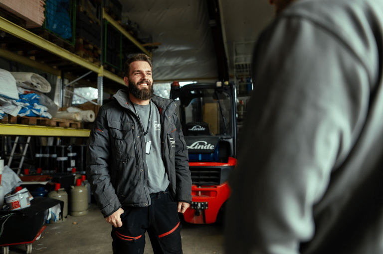 Ein Handwerker spricht lächelnd mit einem Kollegen im Lager und gewinnt neue Kunden.
